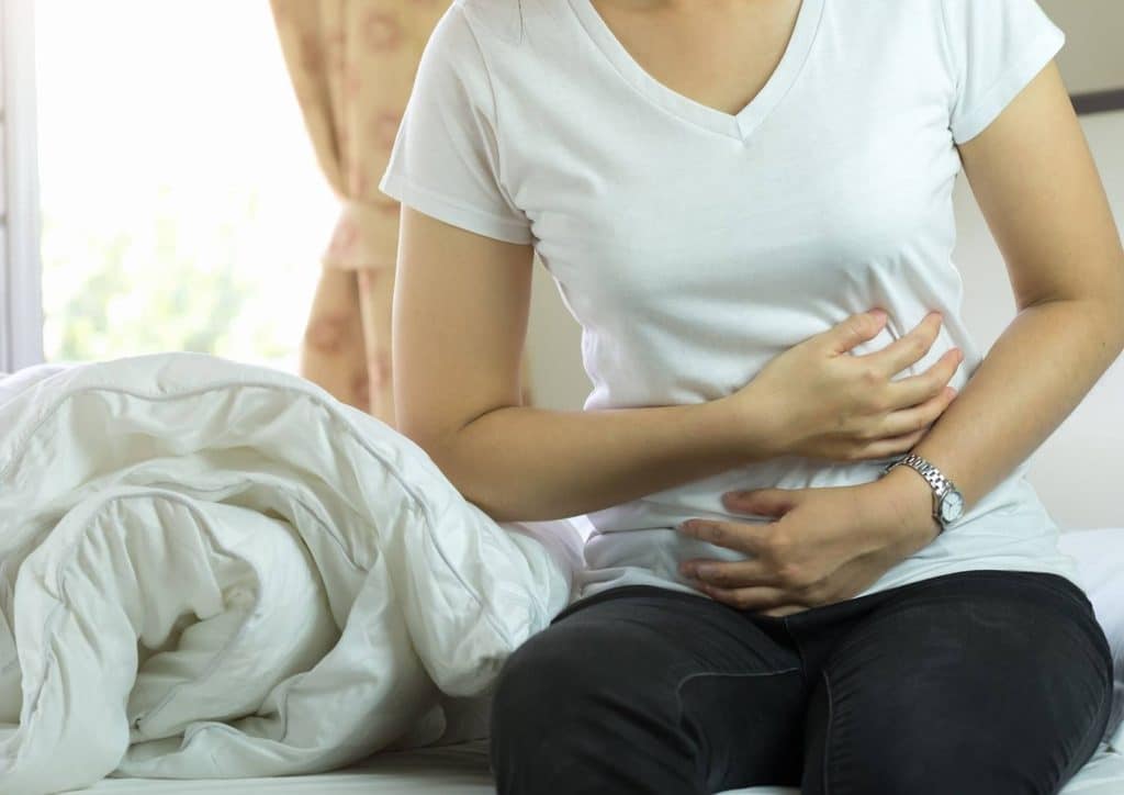 High Fibre Diet for Weight Loss: Why Fibre Keeps You Full 38 A woman sitting on a bed, holding her stomach in discomfort, indicating abdominal pain.