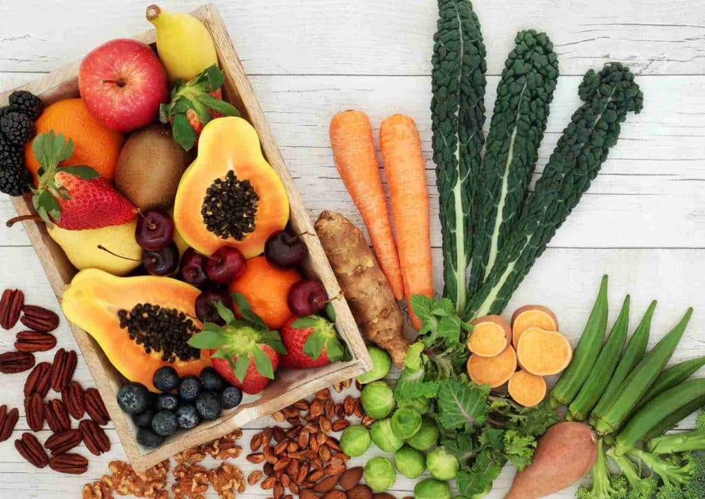 High Fibre Diet for Weight Loss: Why Fibre Keeps You Full 33 A variety of fresh fruits and vegetables are arranged in a wooden crate on a white table, highlighting their natural colours.