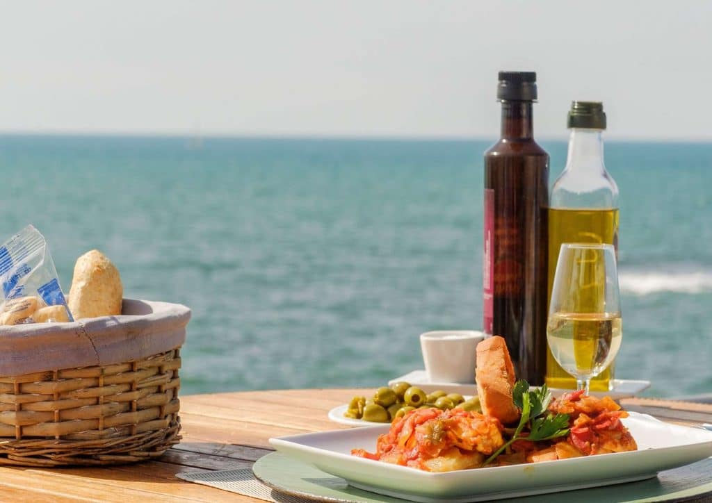 Is the Mediterranean Diet Good for Weight Loss? 15 A plate of gourmet food and a glass of wine on a table, with the ocean visible in the background.