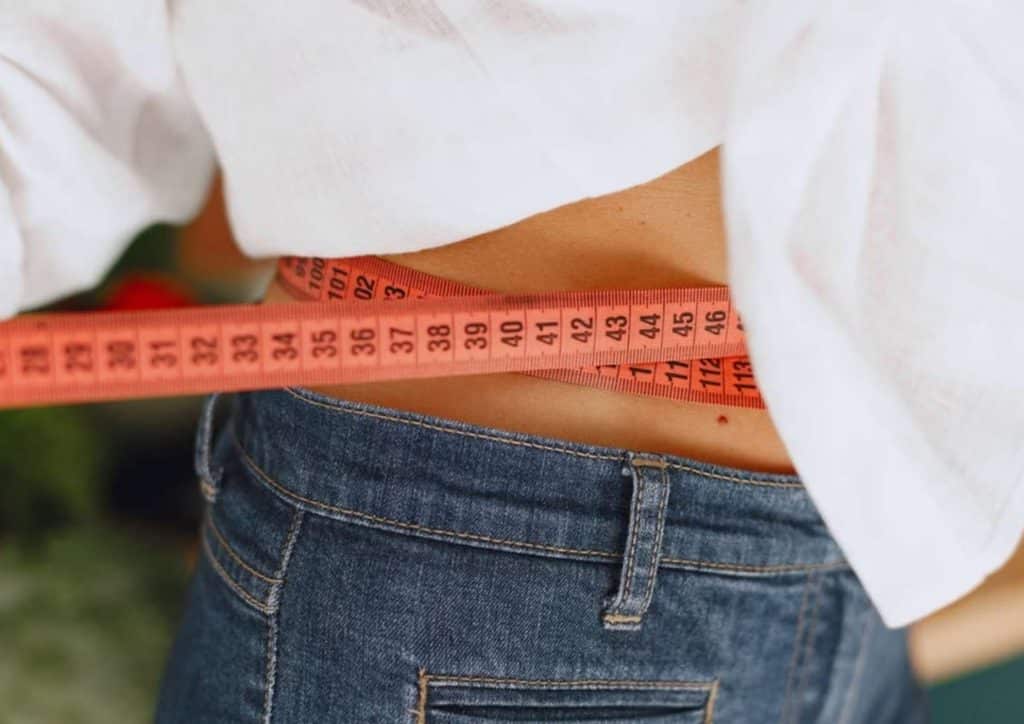 Losing Weight While Breastfeeding: What's Safe and Realistic 51 A woman measuring her waist with a tape measure, focusing on her midsection for fitness or health assessment.