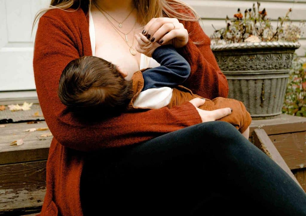 Losing Weight While Breastfeeding: What's Safe and Realistic 25 A woman breastfeeding her baby while seated on a porch, surrounded by a serene outdoor setting.