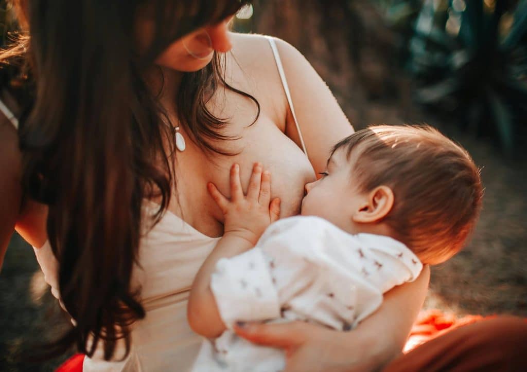 Losing Weight While Breastfeeding: What's Safe and Realistic 64 A woman sits on a park bench, breastfeeding her baby while enjoying the serene outdoor environment.