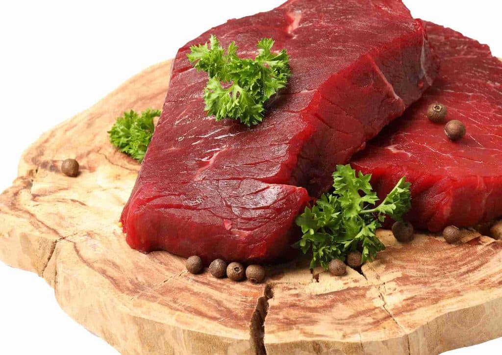 Is Whey Protein Good for Weight Loss? 39 Two pieces of raw beef placed on a wooden cutting board, showcasing their rich red color and marbled texture.