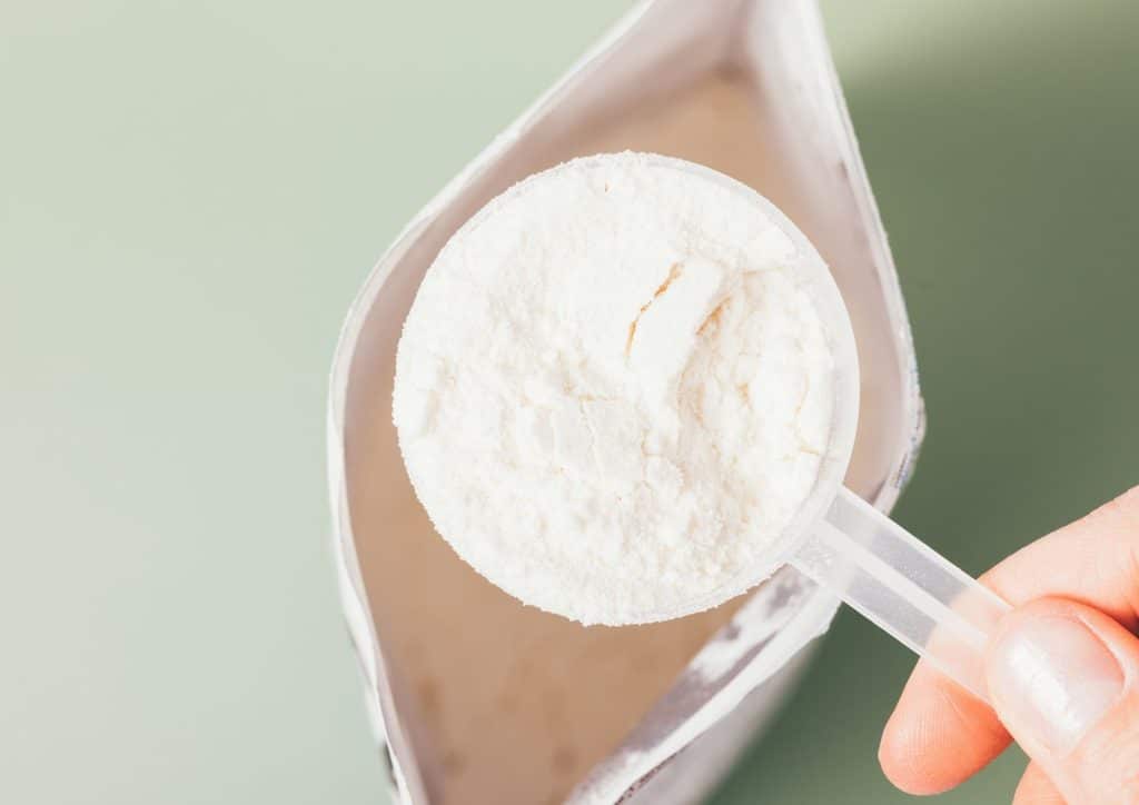 Is Whey Protein Good for Weight Loss? 32 A hand holds a scoop of protein powder in front of an open bag of protein supplement.