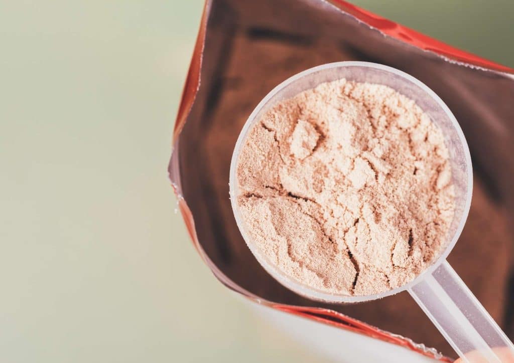 Is Whey Protein Good for Weight Loss? 31 A hand holds a scoop of protein powder in front of an open bag of protein supplement.