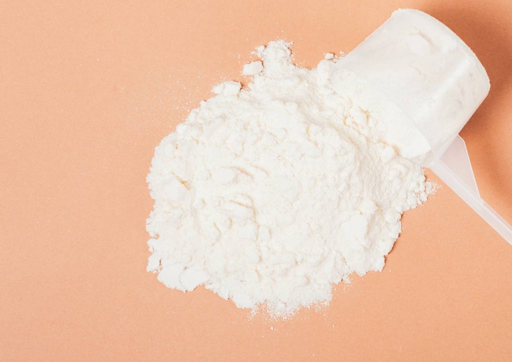 Is Whey Protein Good for Weight Loss? 29 Flour and a measuring spoon placed on a vibrant orange background, highlighting baking ingredients.