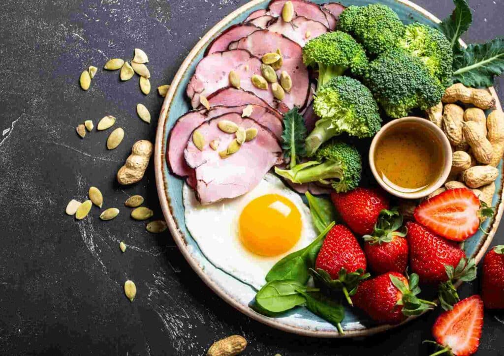 Keto vs Low Carb for Weight Loss: Which Is Better? 19 A plate featuring broccoli, strawberries, eggs, nuts, and a bowl of peanut butter, showcasing a healthy meal.