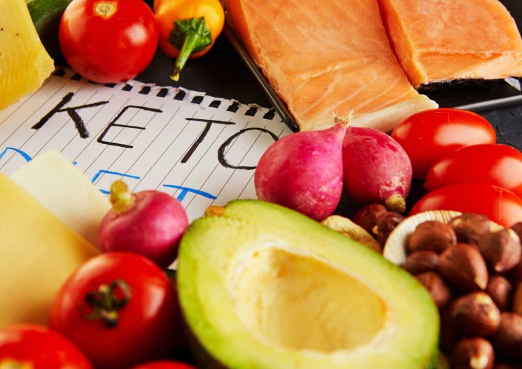 Keto vs Low Carb for Weight Loss: Which Is Better? 12 A variety of keto diet foods including avocados, leafy greens, nuts, and low-carb vegetables arranged on a wooden table.