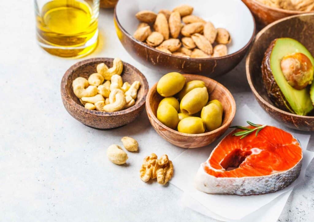 Keto vs Low Carb for Weight Loss: Which Is Better? 29 A variety of healthy foods including nuts, avocado, salmon, and olive oil arranged on a wooden surface.