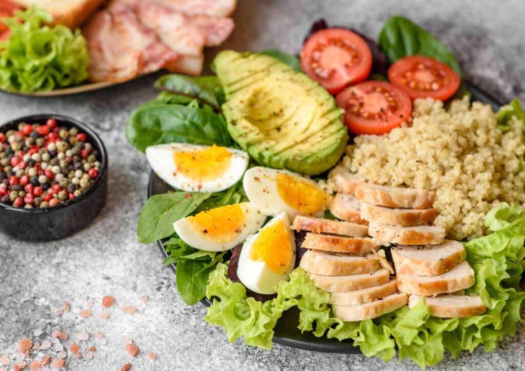 Keto vs Low Carb for Weight Loss: Which Is Better? 3 A plate featuring grilled chicken, sliced avocado, boiled eggs, cherry tomatoes, and mixed greens arranged artfully.