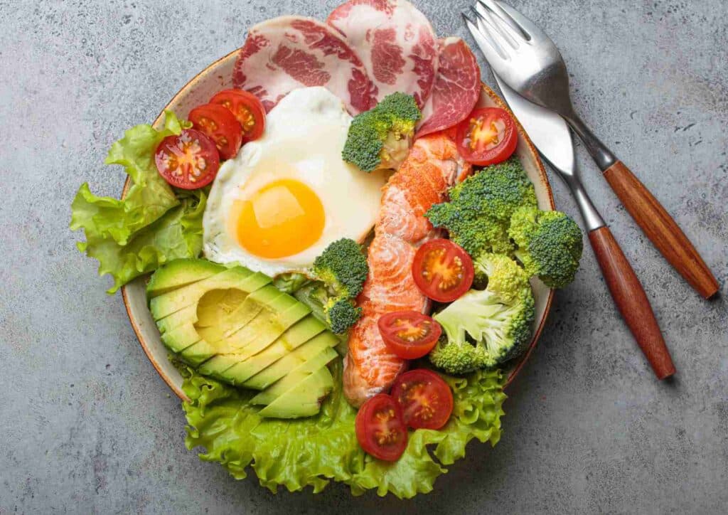 Keto vs Low Carb for Weight Loss: Which Is Better? 4 A plate featuring scrambled eggs, smoked salmon, cherry tomatoes, sliced avocado, and crispy bacon.