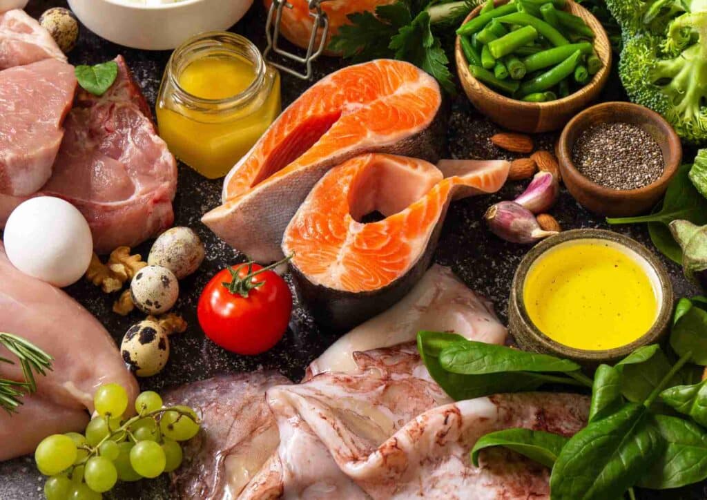 Keto vs Low Carb for Weight Loss: Which Is Better? 20 A variety of foods displayed, including meat, eggs, vegetables, and assorted other items on a wooden surface.