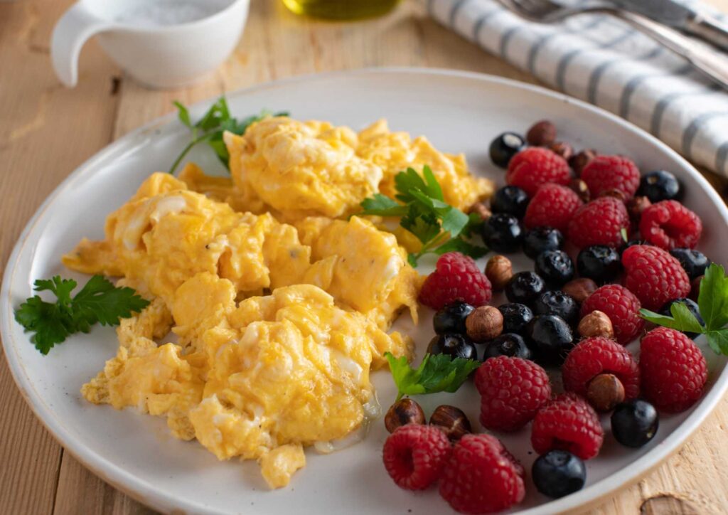 Keto vs Low Carb for Weight Loss: Which Is Better? 21 Scrambled eggs garnished with parsley and served with fresh berries on a white plate.