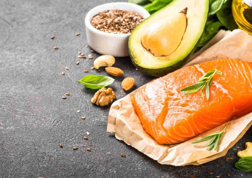 Keto vs Low Carb for Weight Loss: Which Is Better? 27 A vibrant arrangement of salmon, avocado, nuts, and herbs displayed on a black background.