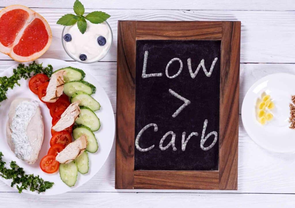 Keto vs Low Carb for Weight Loss: Which Is Better? 39 A variety of low carb diet foods including leafy greens, avocados, nuts, and lean meats arranged on a wooden table.