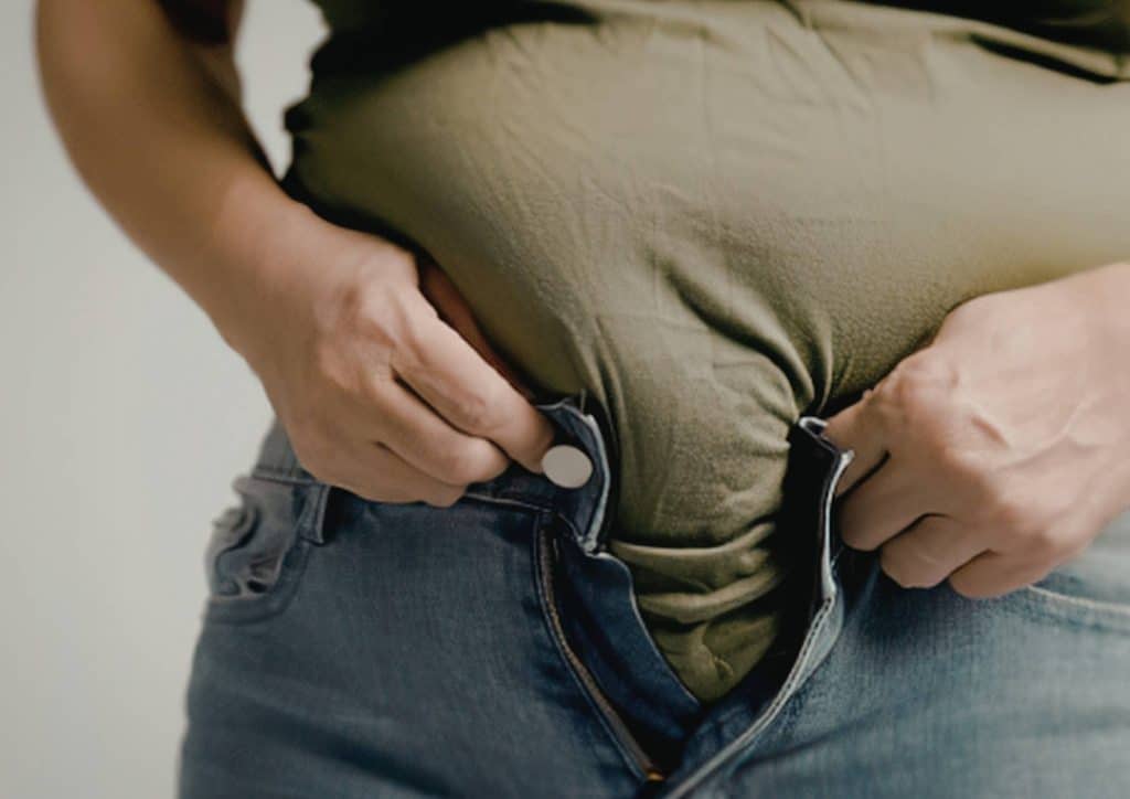Postpartum Weight Loss: A Gentle, Realistic Guide 11 Pregnant woman in jeans gently cradles her belly, showcasing her baby bump with a serene expression.