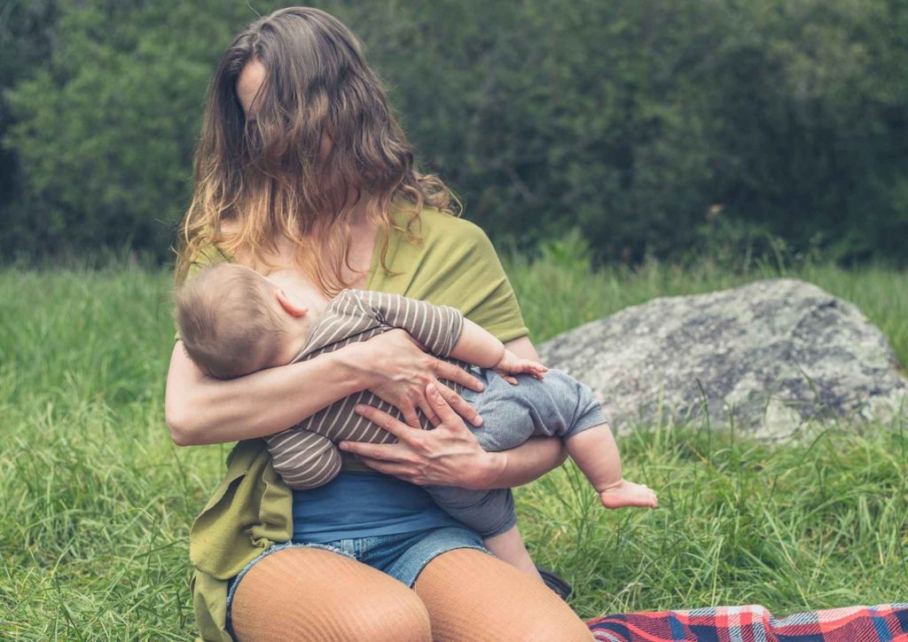 Losing Weight While Breastfeeding: What's Safe and Realistic 43 A woman gently cradles a baby in her arms while sitting on the grass, surrounded by a serene outdoor setting.
