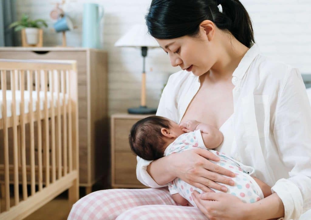 Losing Weight While Breastfeeding: What's Safe and Realistic 41 A woman gently breastfeeding her baby while seated beside a crib, creating a nurturing atmosphere.
