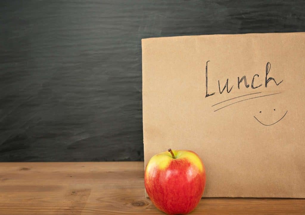 Healthy Lunches for Weight Loss: Work and Home Ideas 20 Lunch bag featuring a smiley face and an apple, placed on a wooden table.