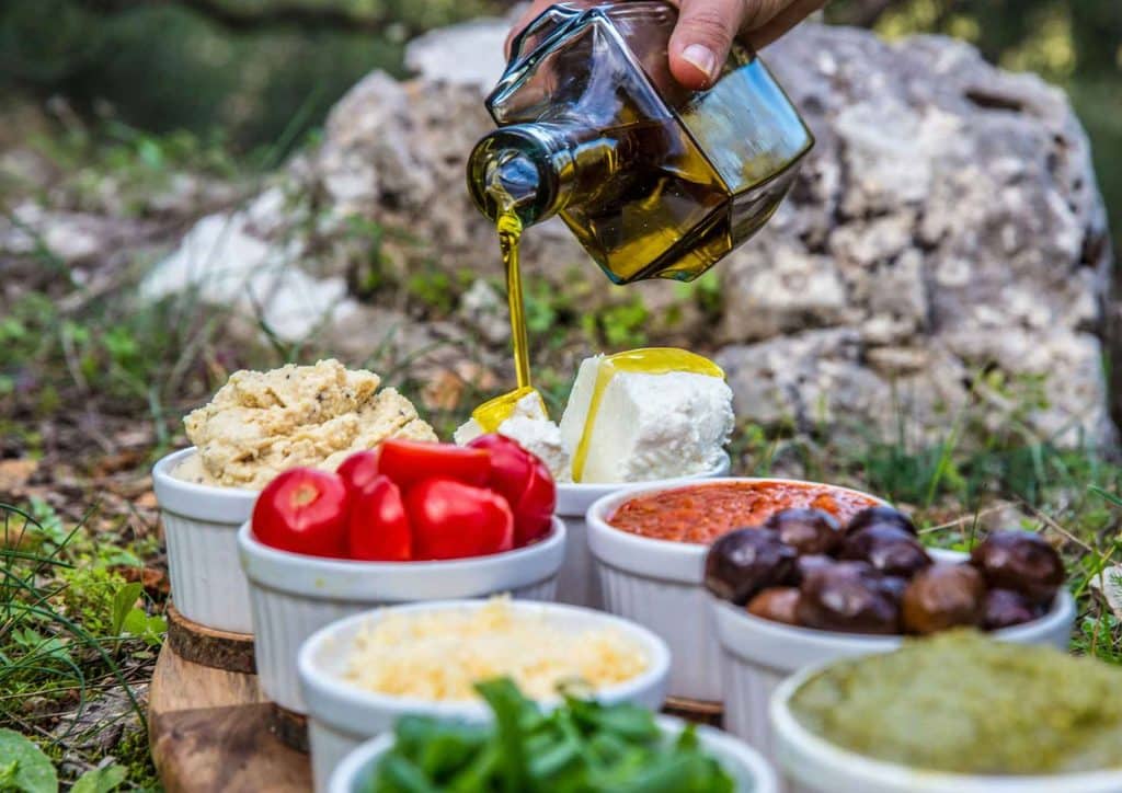 Is the Mediterranean Diet Good for Weight Loss? 23 A person pouring olive oil from a bottle into several bowls of food on a kitchen counter.