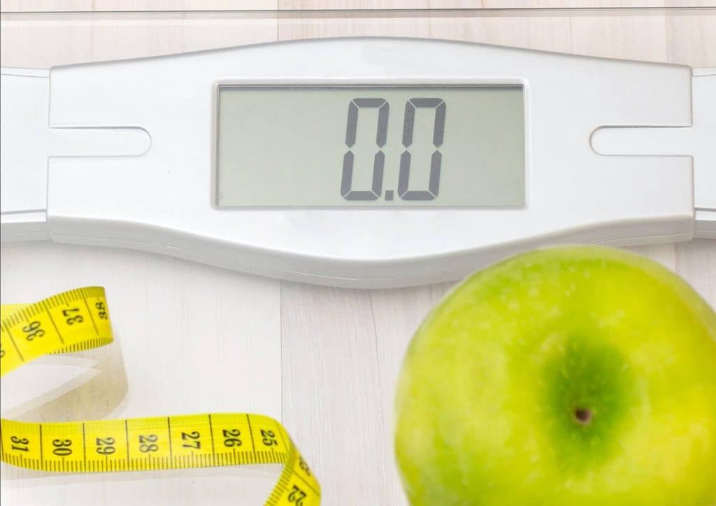 What Is a Balanced Diet for Weight Loss? 19 A green apple placed beside a scale and a measuring tape, illustrating weight and measurement concepts.