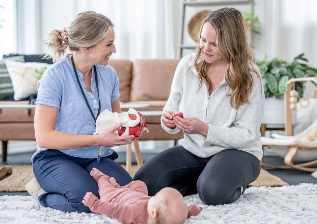 Postpartum Weight Loss: A Gentle, Realistic Guide 35 Two women sit on the floor, smiling and interacting with a baby between them.