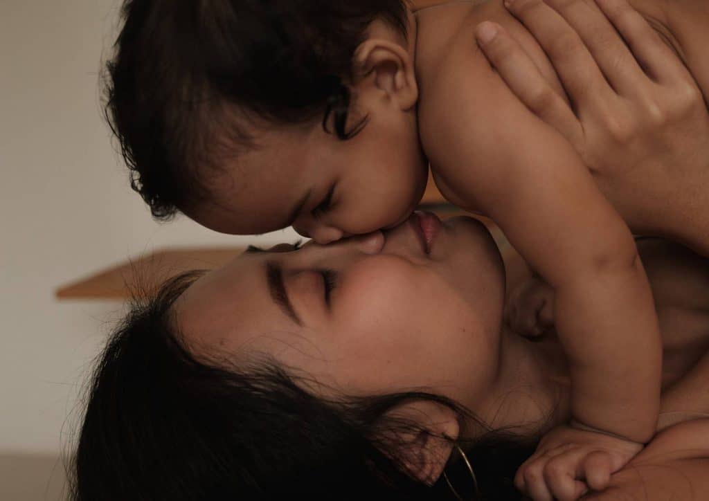 Postpartum Weight Loss: A Gentle, Realistic Guide 37 A woman lovingly kisses a baby she is holding in her arms, showcasing a tender moment of affection.