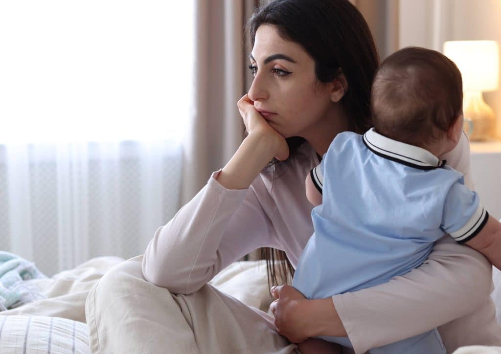 Postpartum Weight Loss: A Gentle, Realistic Guide 36 A woman sits on a bed, gently holding a baby in her arms, both appearing calm and content.