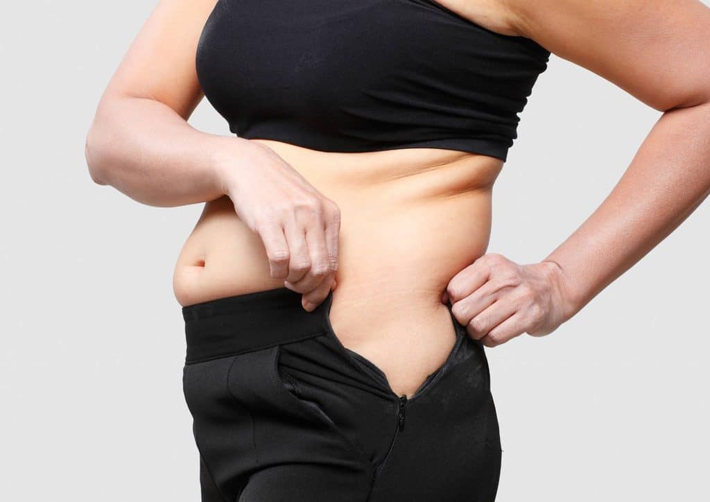 Postpartum Weight Loss: A Gentle, Realistic Guide 25 A woman stands with her pants lowered, revealing her stomach in a casual setting.
