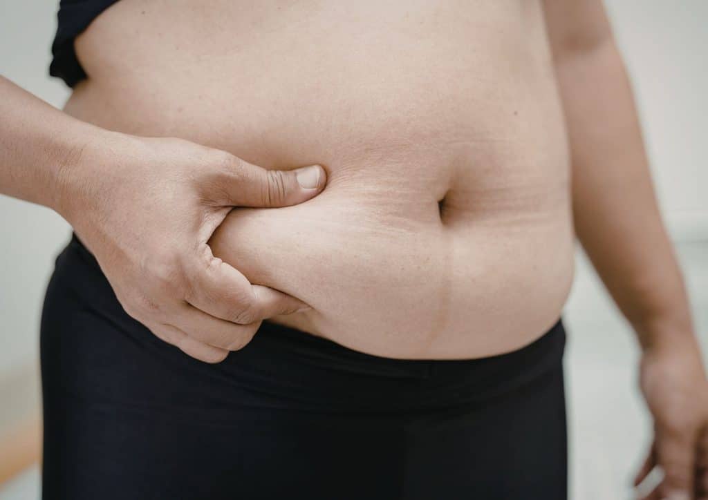 Postpartum Weight Loss: A Gentle, Realistic Guide 28 A woman stands with her hands on her stomach, expressing discomfort or concern.