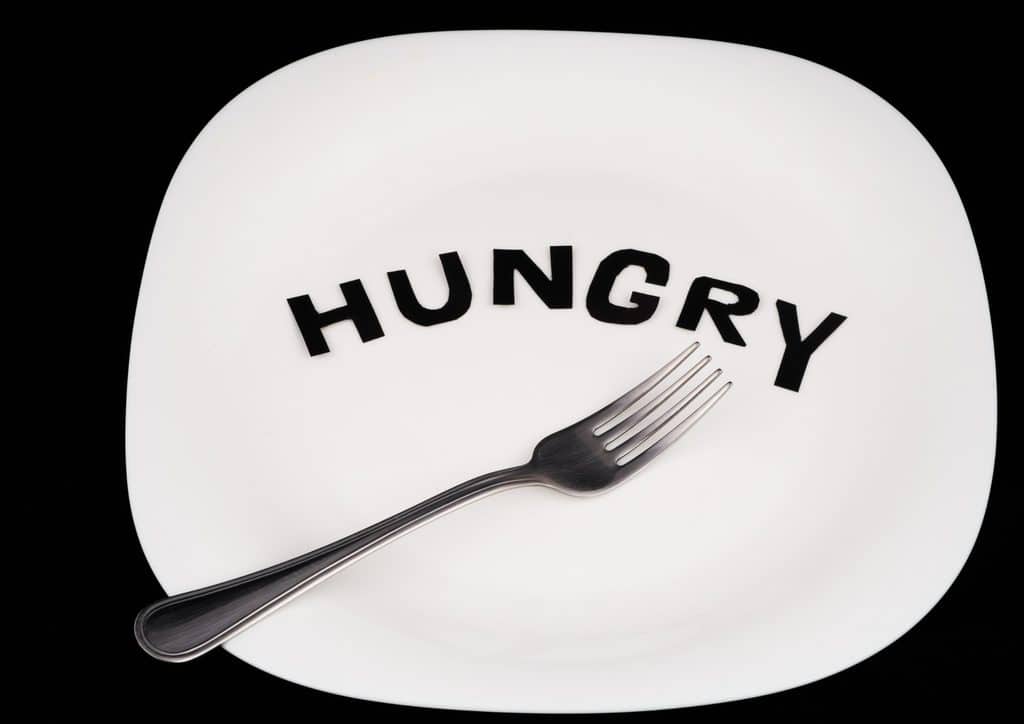 Postpartum Weight Loss: A Gentle, Realistic Guide 26 A fork and knife rest on a white plate, with the word "hungry" written in bold black letters nearby.