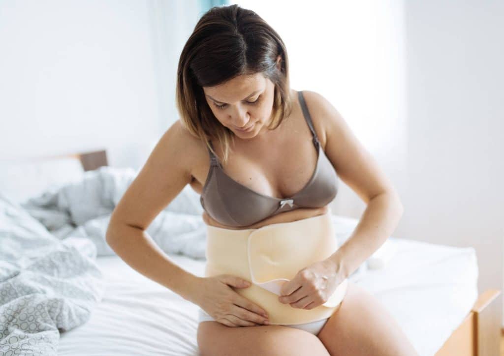 Postpartum Weight Loss: A Gentle, Realistic Guide 30 A woman in a bra top gently holds her stomach, conveying a sense of contemplation or discomfort.