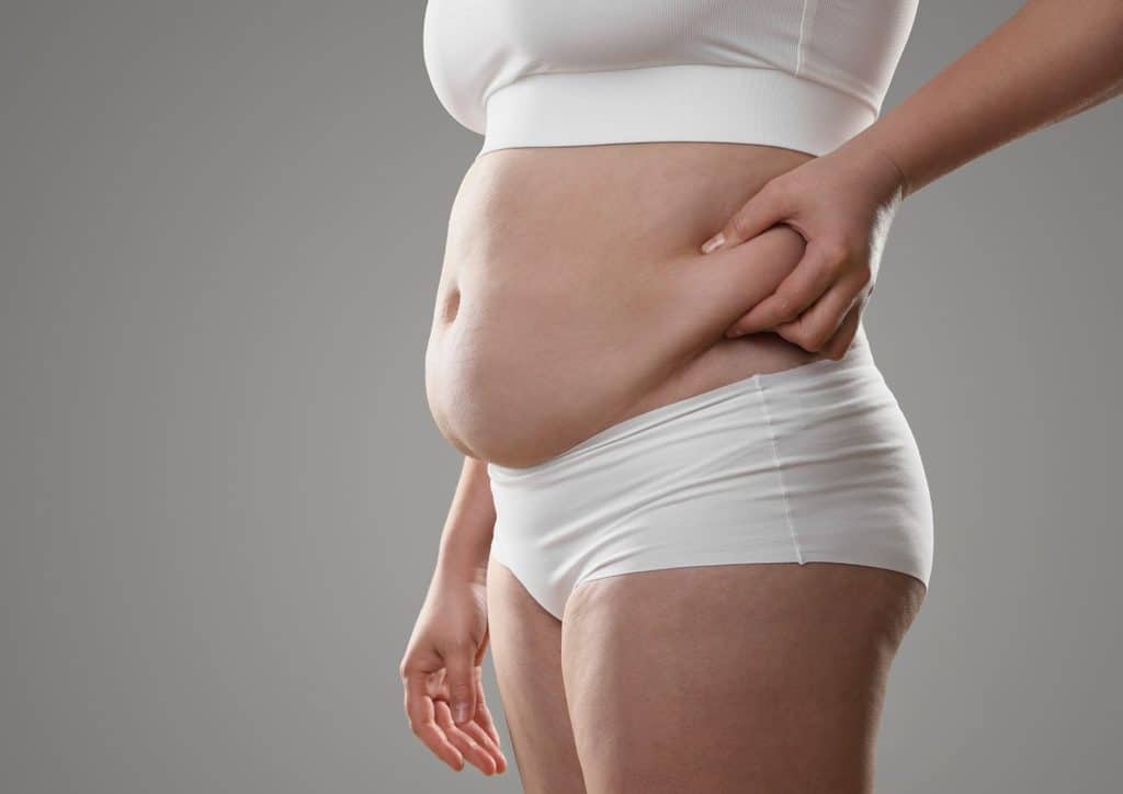 Postpartum Weight Loss: A Gentle, Realistic Guide 32 A woman wearing a white top and shorts stands outdoors, smiling at the camera.