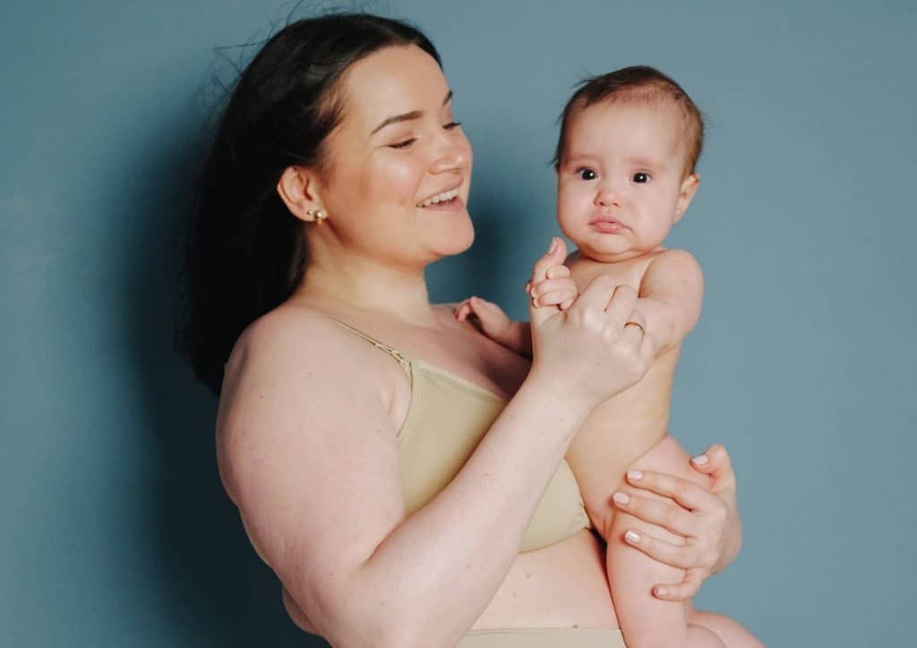 Postpartum Weight Loss: A Gentle, Realistic Guide 6 A woman in a bra and underwear gently holds a baby, showcasing a moment of tenderness and maternal care.