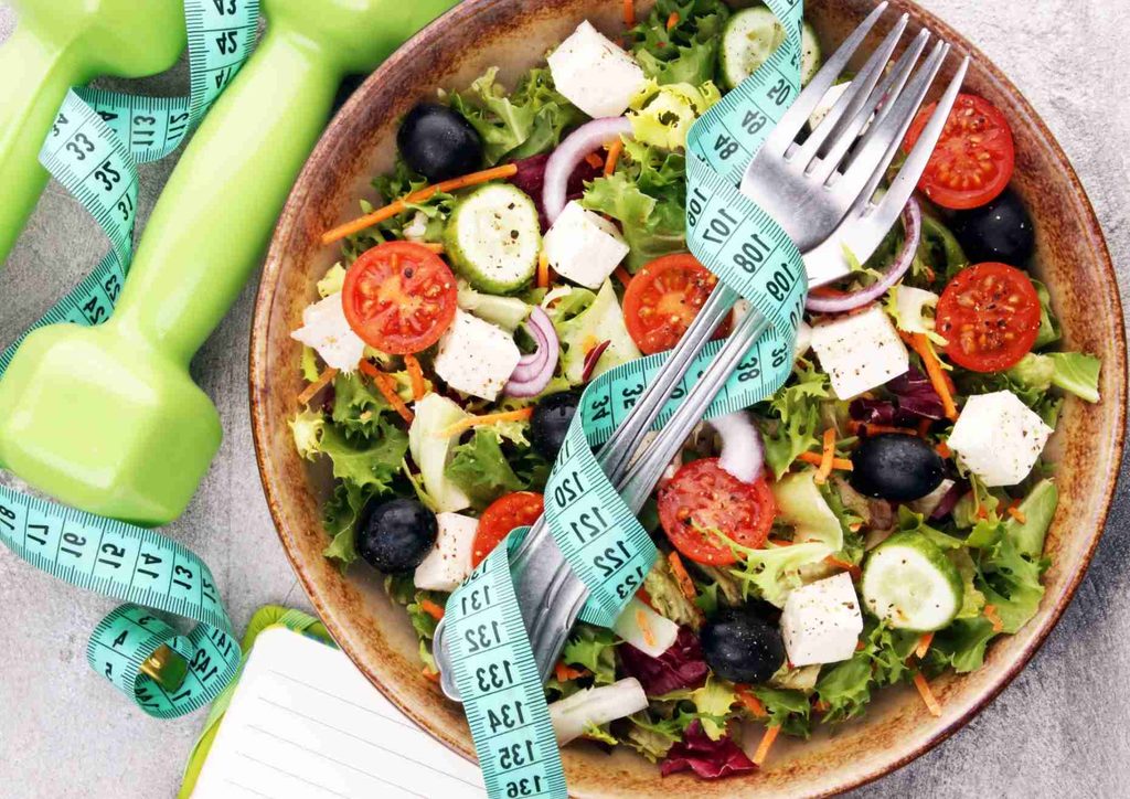 Easy Meals for Weight Loss When You're Short on Time 28 A colourful salad with various vegetables alongside a measuring tape, symbolising healthy eating and portion control.