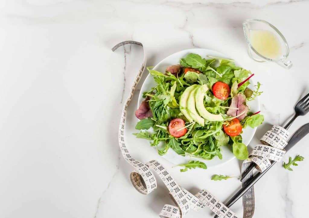 Easy Meals for Weight Loss When You're Short on Time 25 A plate of salad accompanied by a measuring tape, symbolising health and portion control.