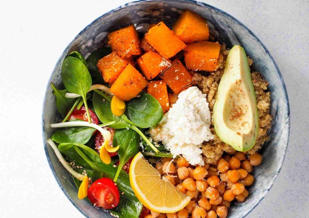 Easy Meals for Weight Loss When You're Short on Time 24 A bowl filled with chickpeas, fresh spinach, sliced avocado, and a wedge of lemon, showcasing a healthy meal option.