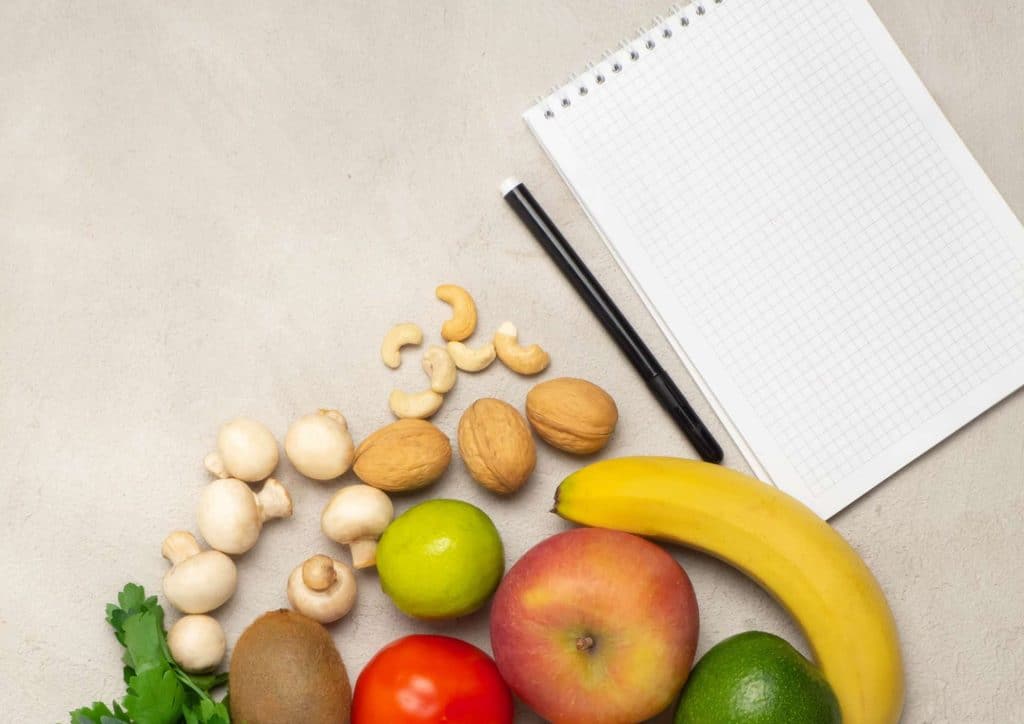 Healthy Meal Plans for Weight Loss: How to Build One That Lasts 33 A notebook, assorted fruits and vegetables, and a pen arranged on a wooden surface.