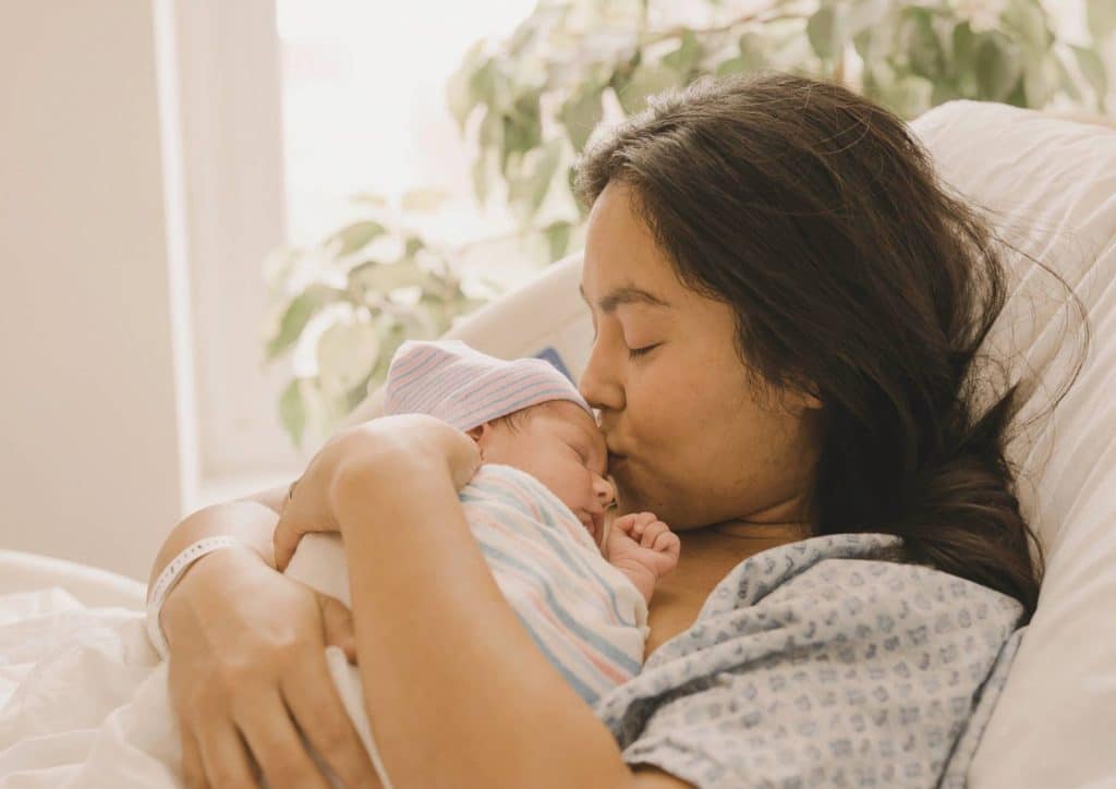 Postpartum Weight Loss: A Gentle, Realistic Guide 10 A woman gently cradles her newborn in bed, both appearing calm and content in a cozy setting.