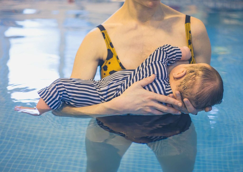 Losing Weight While Breastfeeding: What's Safe and Realistic 66 A woman gently holds a baby in her arms while standing in a swimming pool, both smiling and enjoying the water.