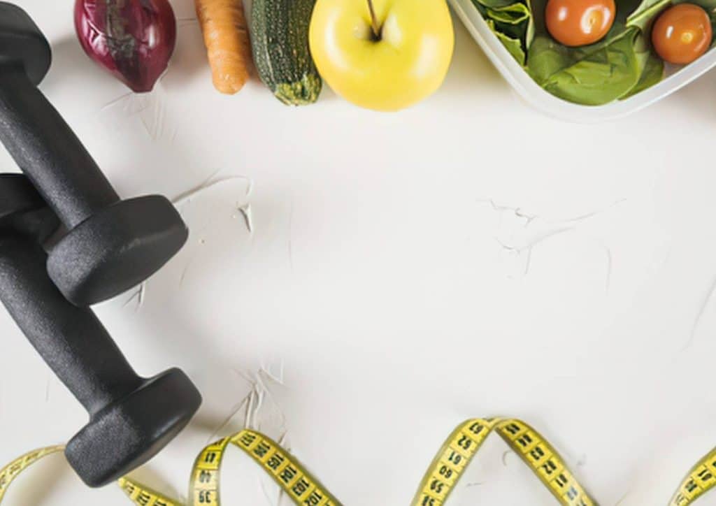 Easy Meals for Weight Loss When You're Short on Time 21 A white table displays a measuring tape, a box of vegetables, and a pair of dumbbells, suggesting a fitness and nutrition theme.