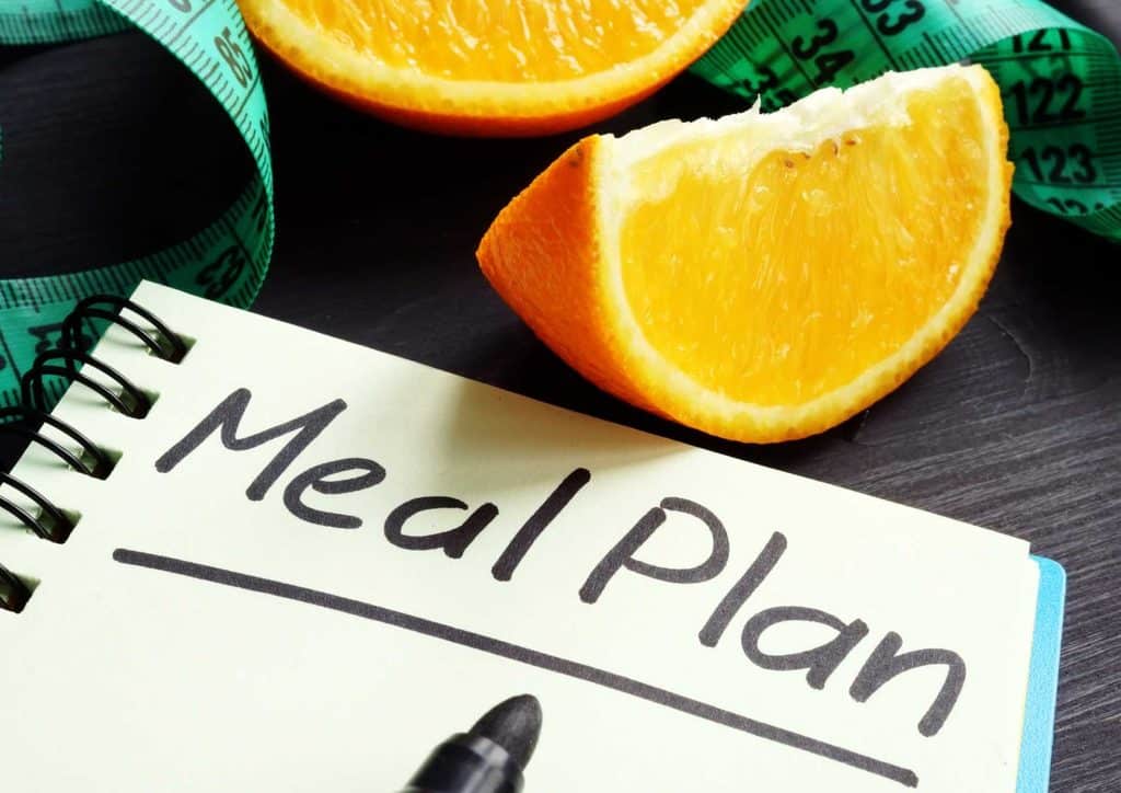Healthy Meal Plans for Weight Loss: How to Build One That Lasts 36 A notebook displaying a meal plan, with an orange and measuring tape nearby, representing nutrition and fitness tracking.