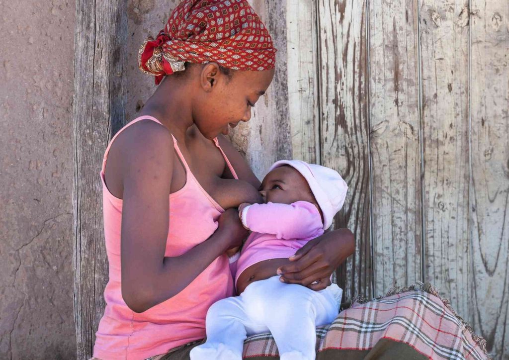 Losing Weight While Breastfeeding: What's Safe and Realistic 75 A woman seated on a bench, gently holding a baby in her arms, both appearing relaxed and content.