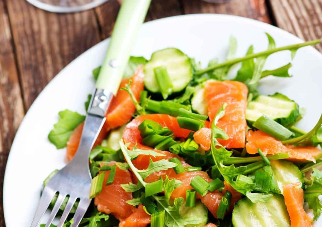 Easy Meals for Weight Loss When You're Short on Time 20 A white plate holds a salmon salad featuring cucumber and green leafy vegetables.