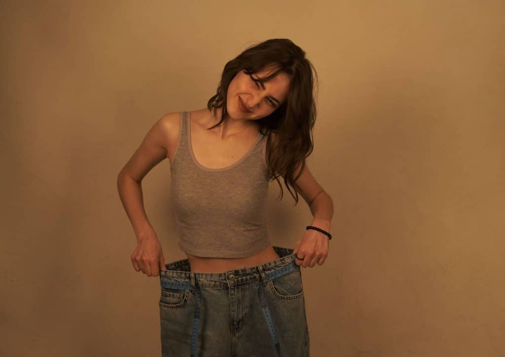 High Fibre Diet for Weight Loss: Why Fibre Keeps You Full 5 A woman wearing jeans stands confidently in front of a textured wall, showcasing a casual yet stylish appearance.