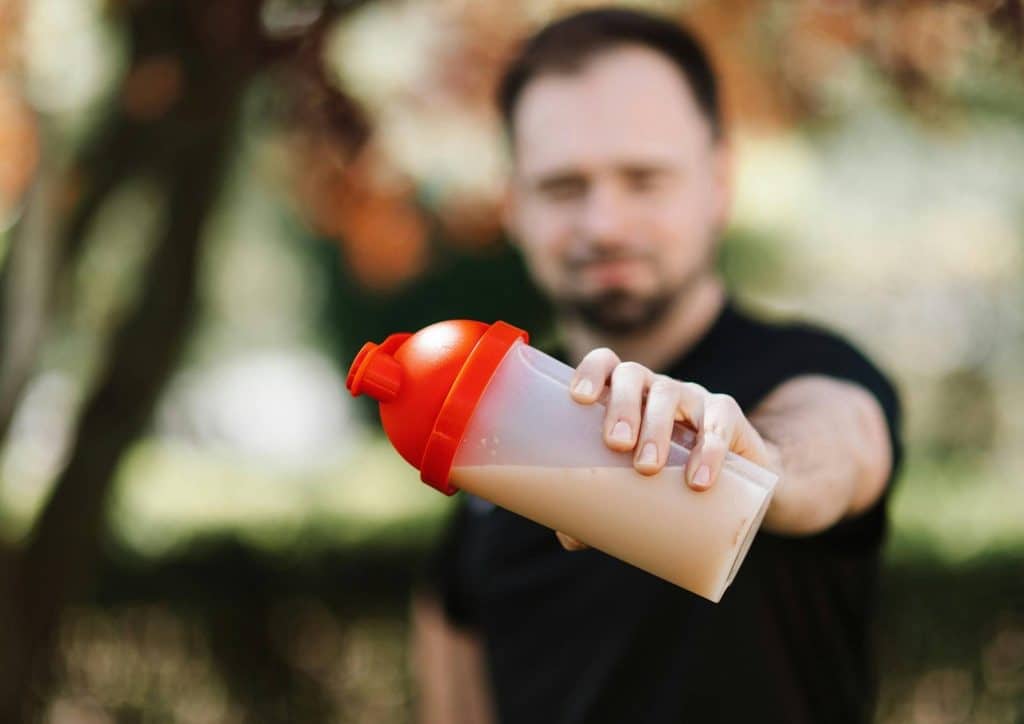 Is Whey Protein Good for Weight Loss? 25 A man holding a protein shake in a clear cup, smiling while standing in a bright, modern kitchen.