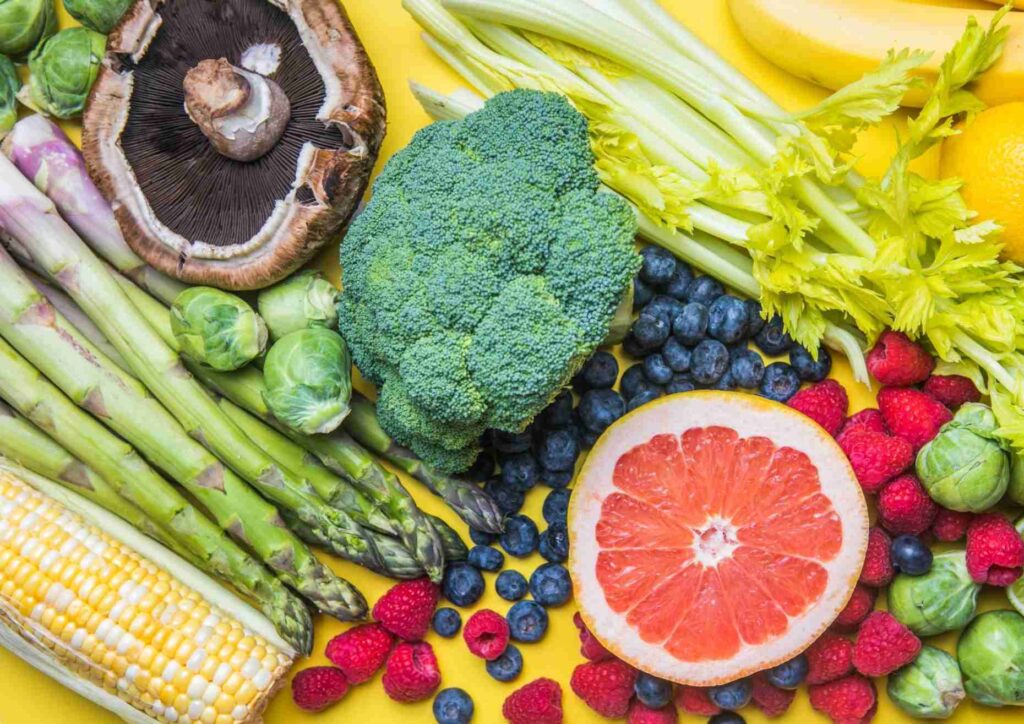 High Fibre Diet for Weight Loss: Why Fibre Keeps You Full 17 Various fruits and vegetables artistically arranged against a vibrant yellow backdrop.