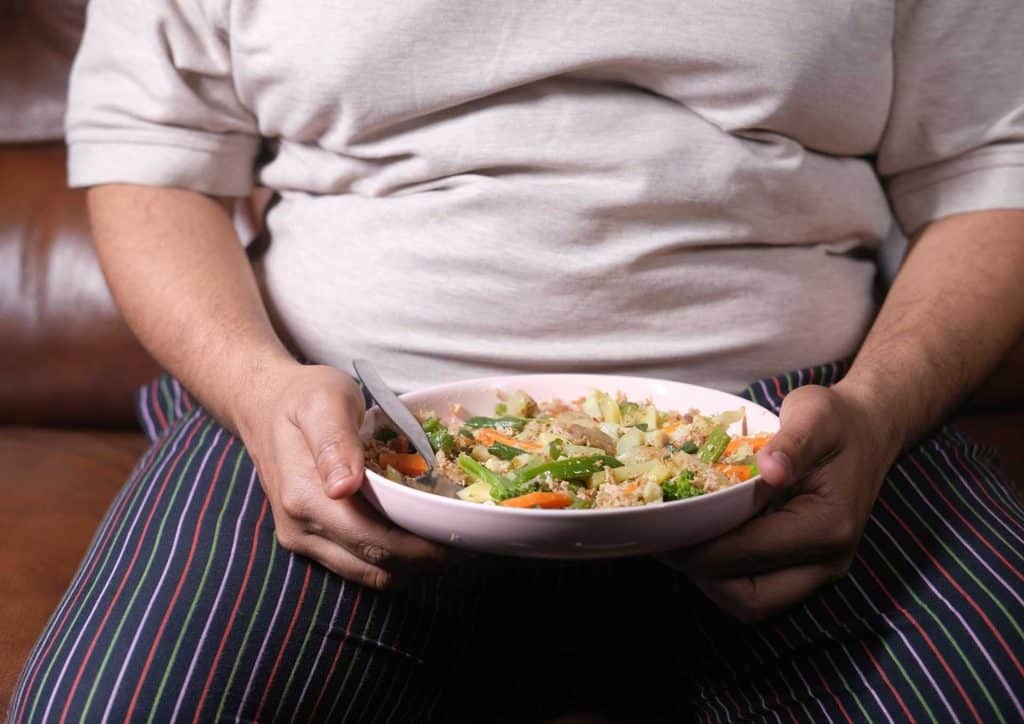 Easy Meals for Weight Loss When You're Short on Time 17 A man sits on a couch, holding a bowl of food, appearing relaxed and engaged in his surroundings