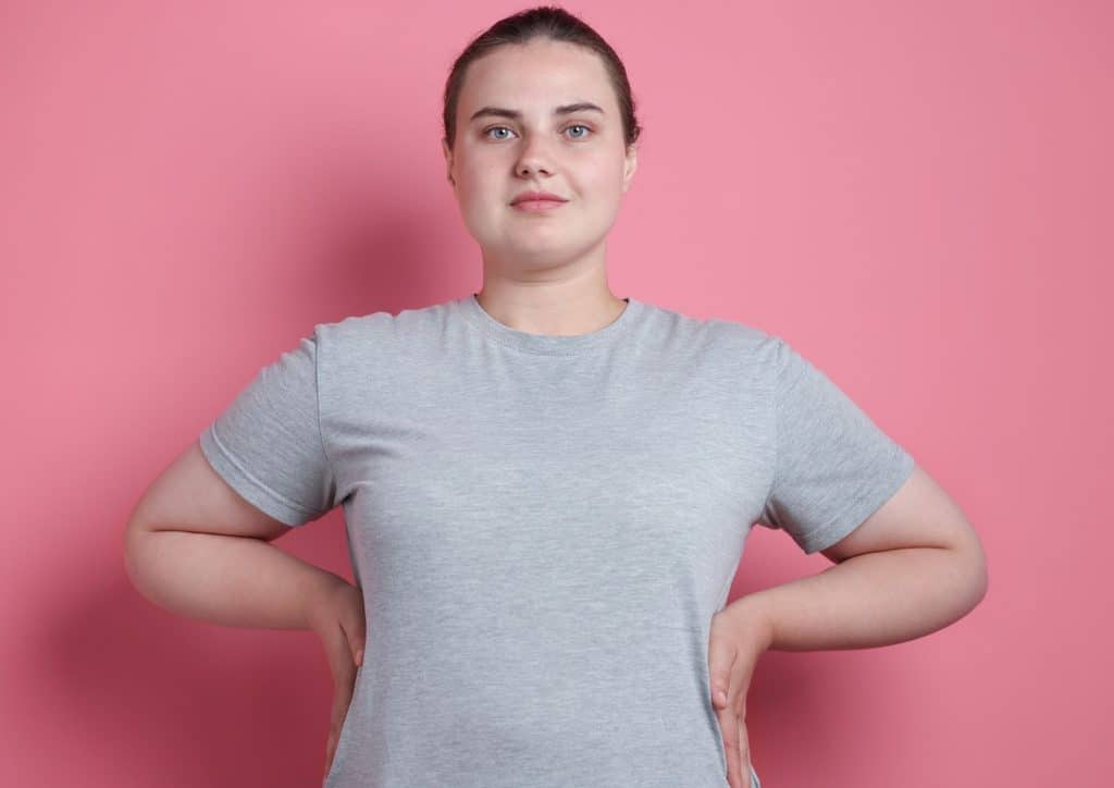 Vegetarian Diet for Weight Loss: How to Get It Right 55 A woman wearing a gray t-shirt stands confidently against a vibrant pink background.