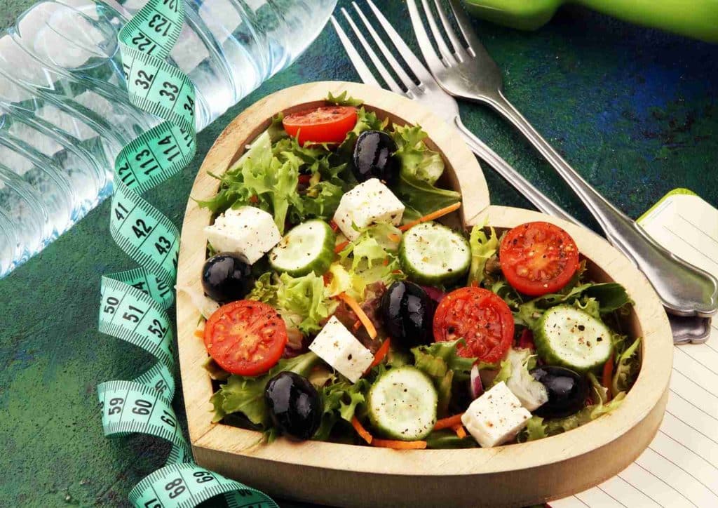Easy Meals for Weight Loss When You're Short on Time 14 Heart-shaped salad made of colorful vegetables, accompanied by a measuring tape, symbolising healthy eating and fitness.